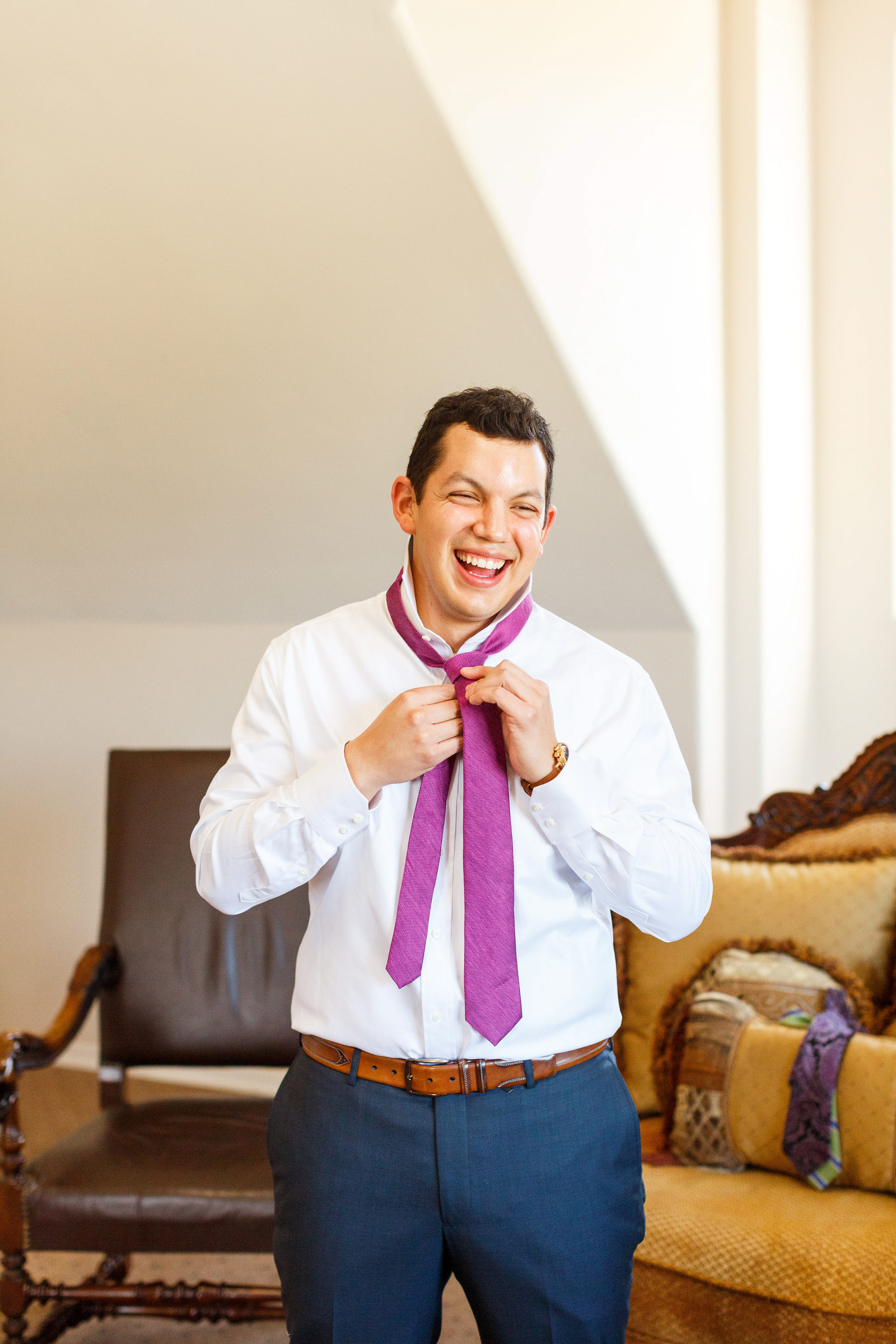 Groom laughing and putting on his tie at Spanish Oaks Ranch